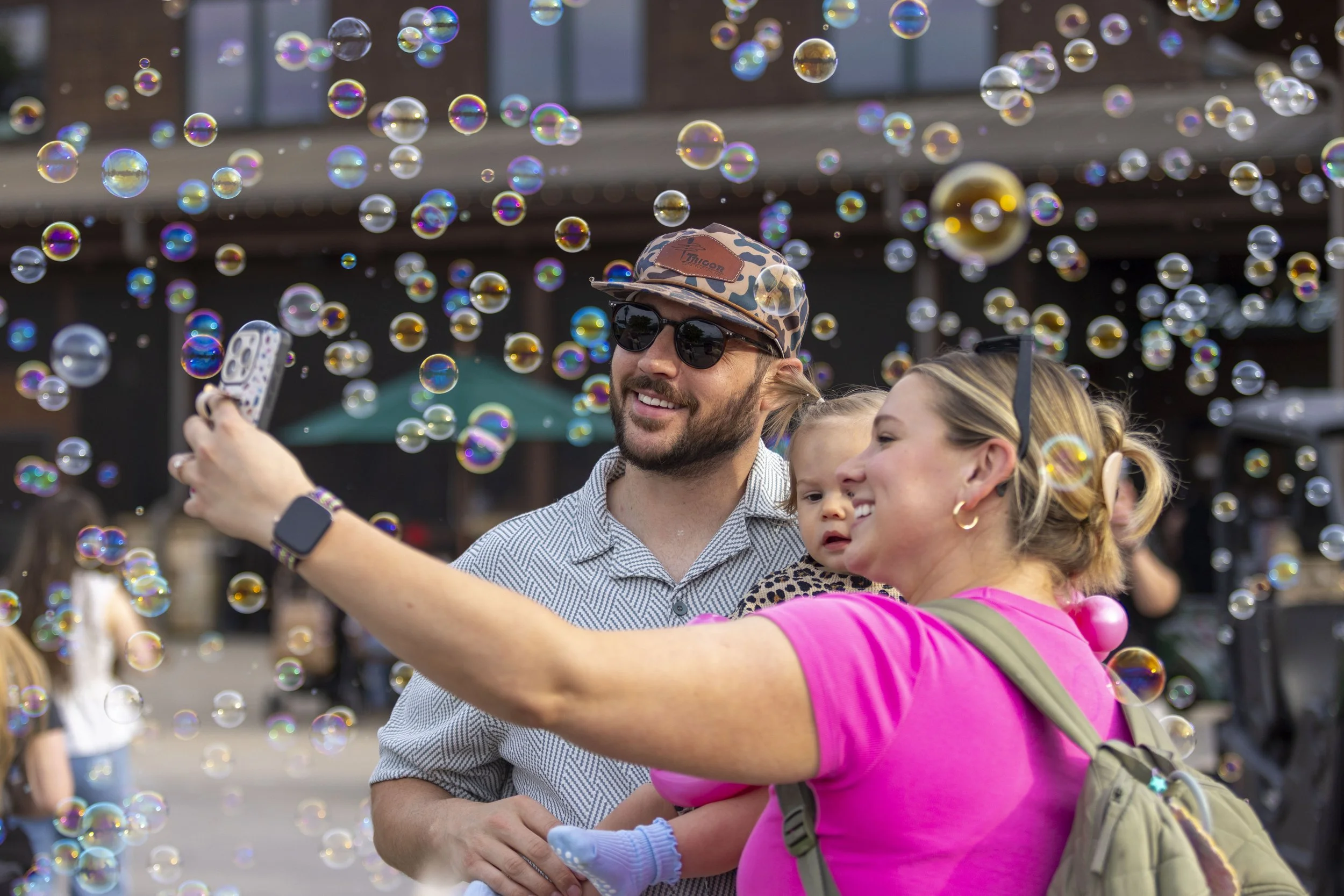 Children playing with bubbles outdoors, smiling and reaching for the bubbles.
