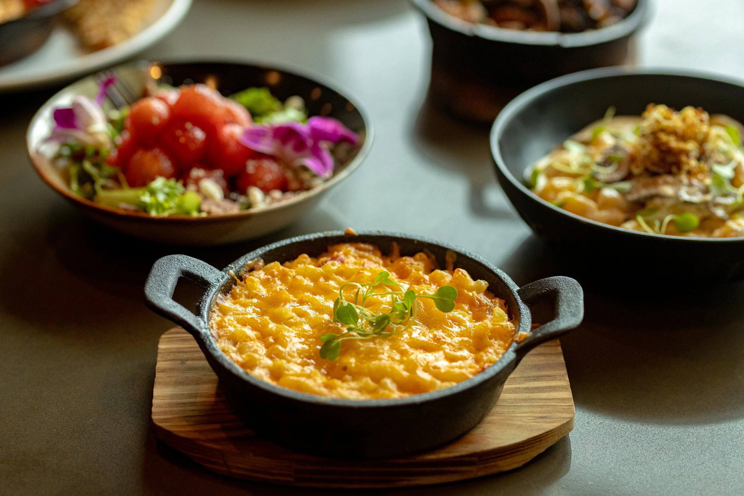 Small cast iron skillet filled with cheesy baked dish garnished with microgreens, placed on a wooden board.