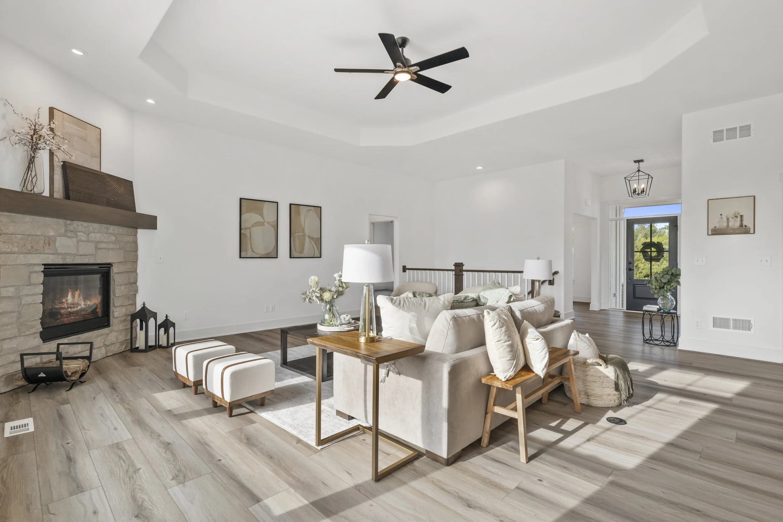 Living room with white walls, a stone fireplace, beige sofa, wooden coffee table, wall art, and a ceiling fan.