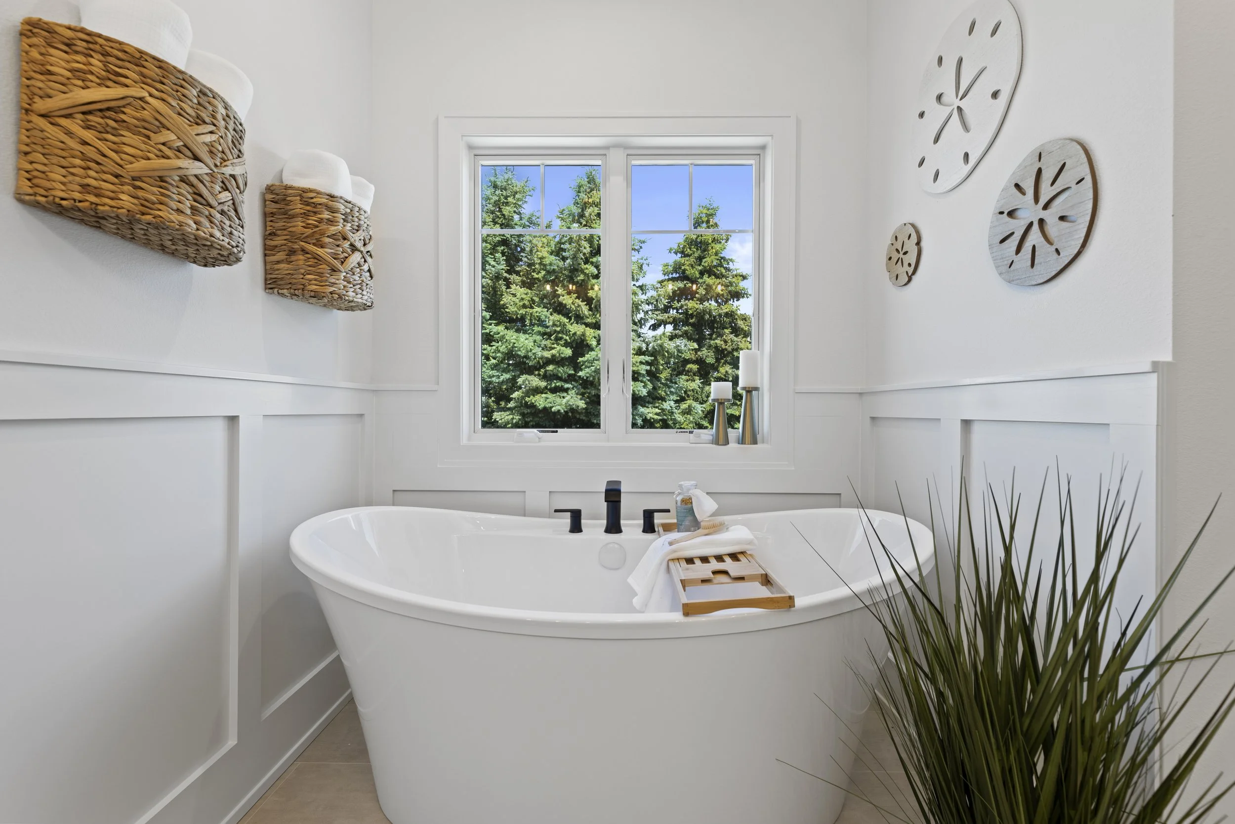 Bathroom with a freestanding bathtub in front of a window with a view of trees, decorated with wall art and baskets on the wall.