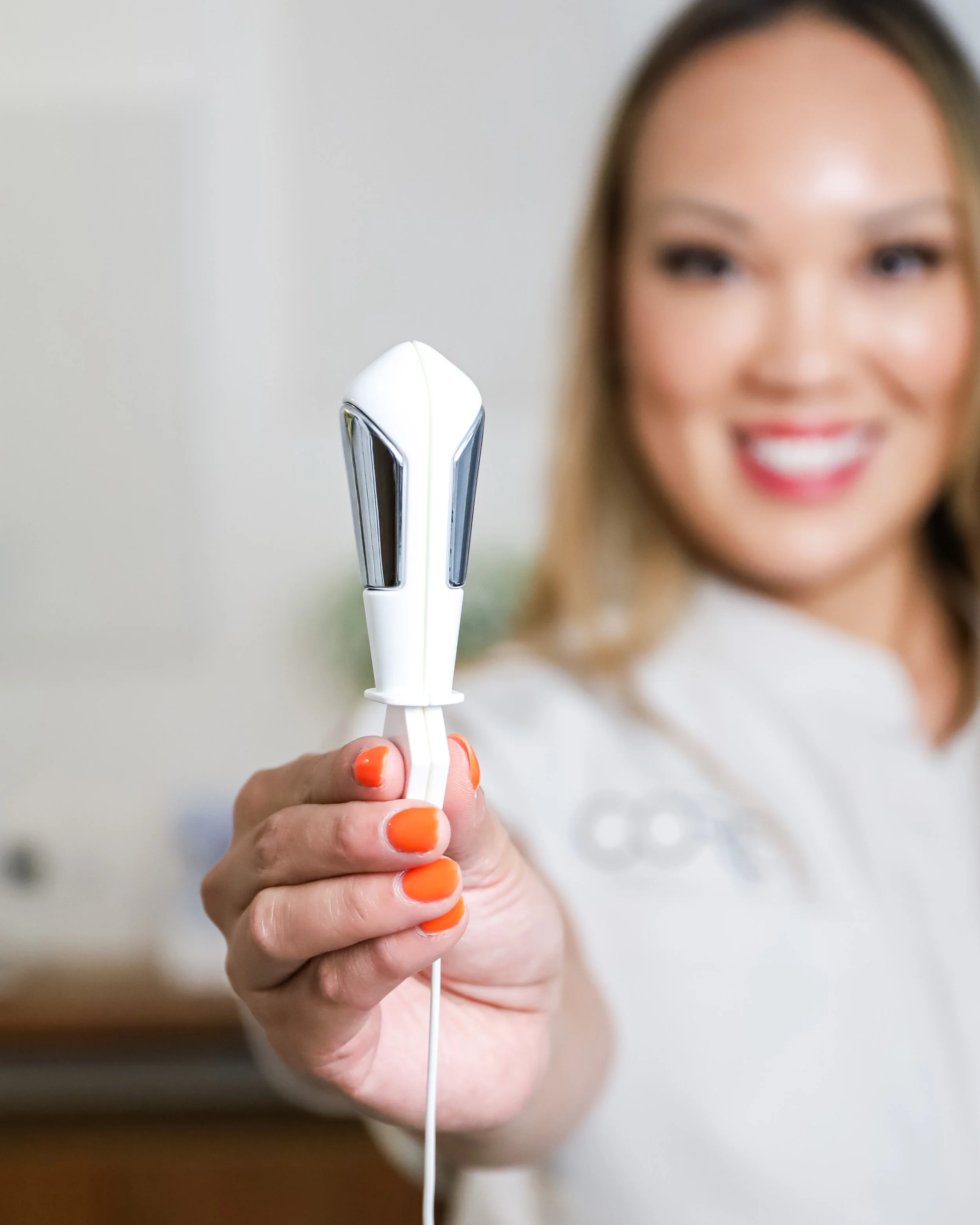 Person holding a white handheld beauty device with orange nail polish.