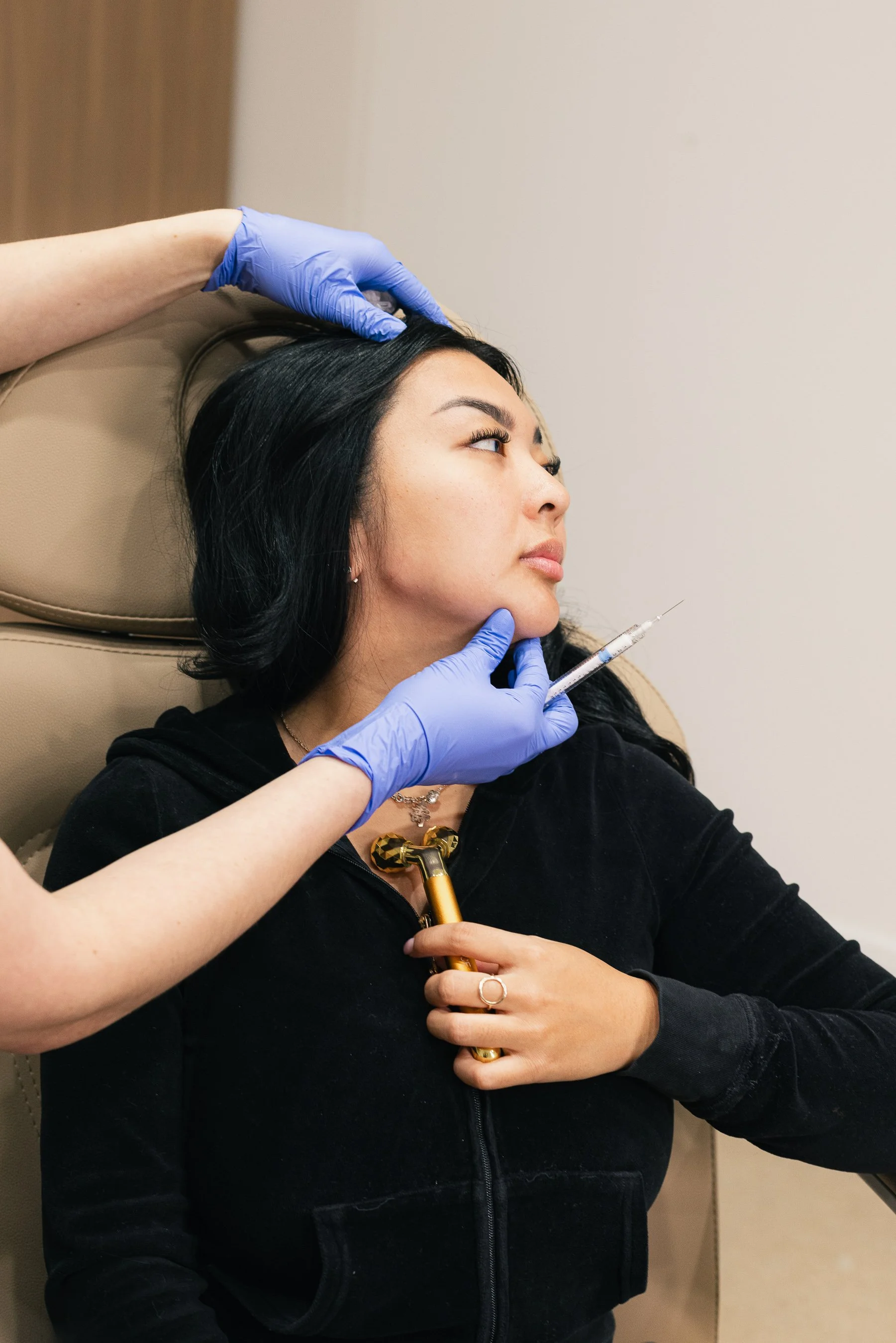 A woman receiving a cosmetic injection in her chin by a professional wearing blue gloves.