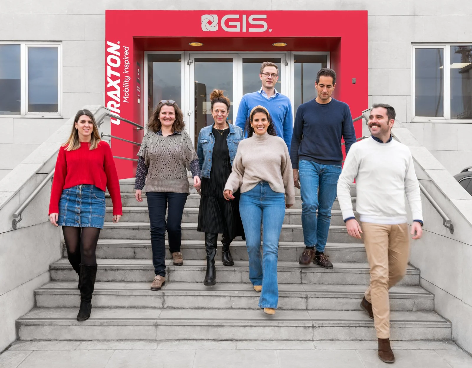 Grupo de empleados sonrientes bajando las escaleras en la entrada de la empresa, cierre humano del reportaje.