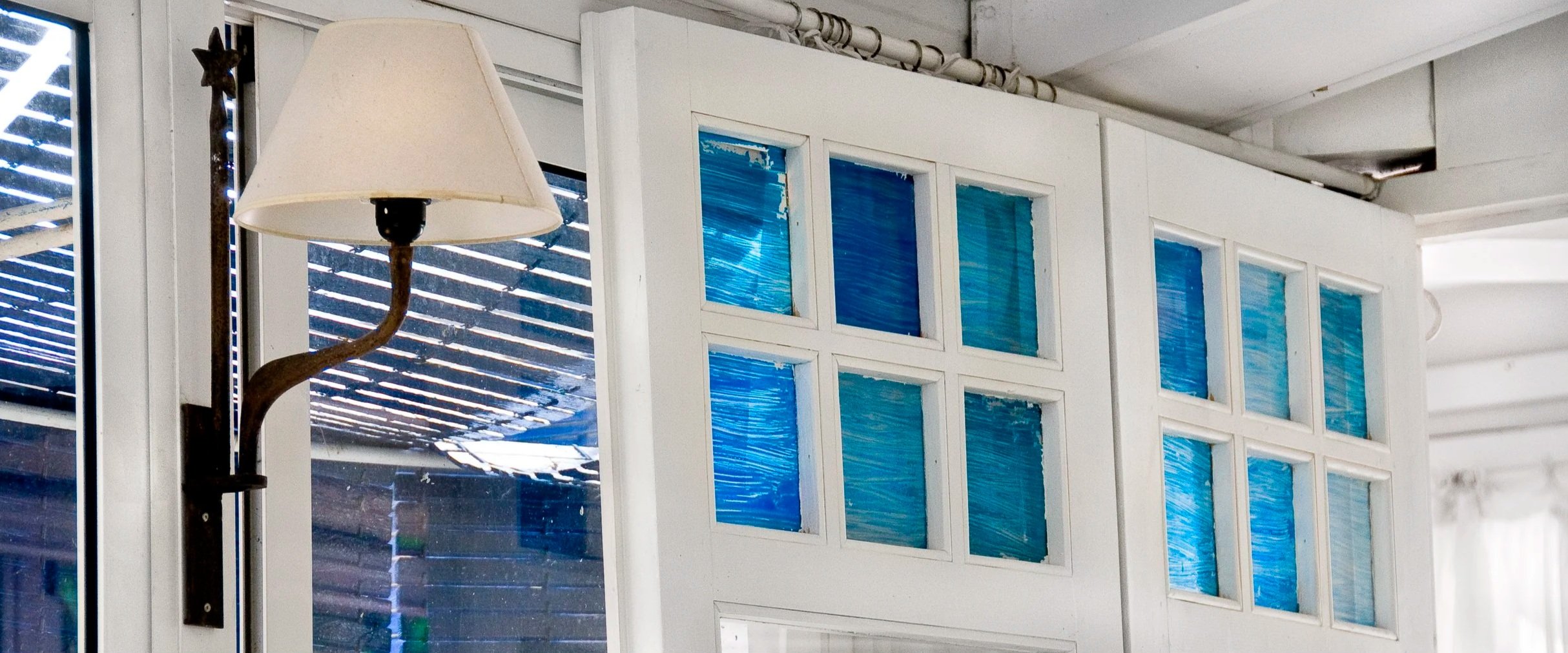 Interior del restaurante El Jardinet (Hotel César, Vilanova i la Geltrú) con lámpara en primer plano y puerta blanca con vidrios azules al fondo, atmósfera mediterránea.