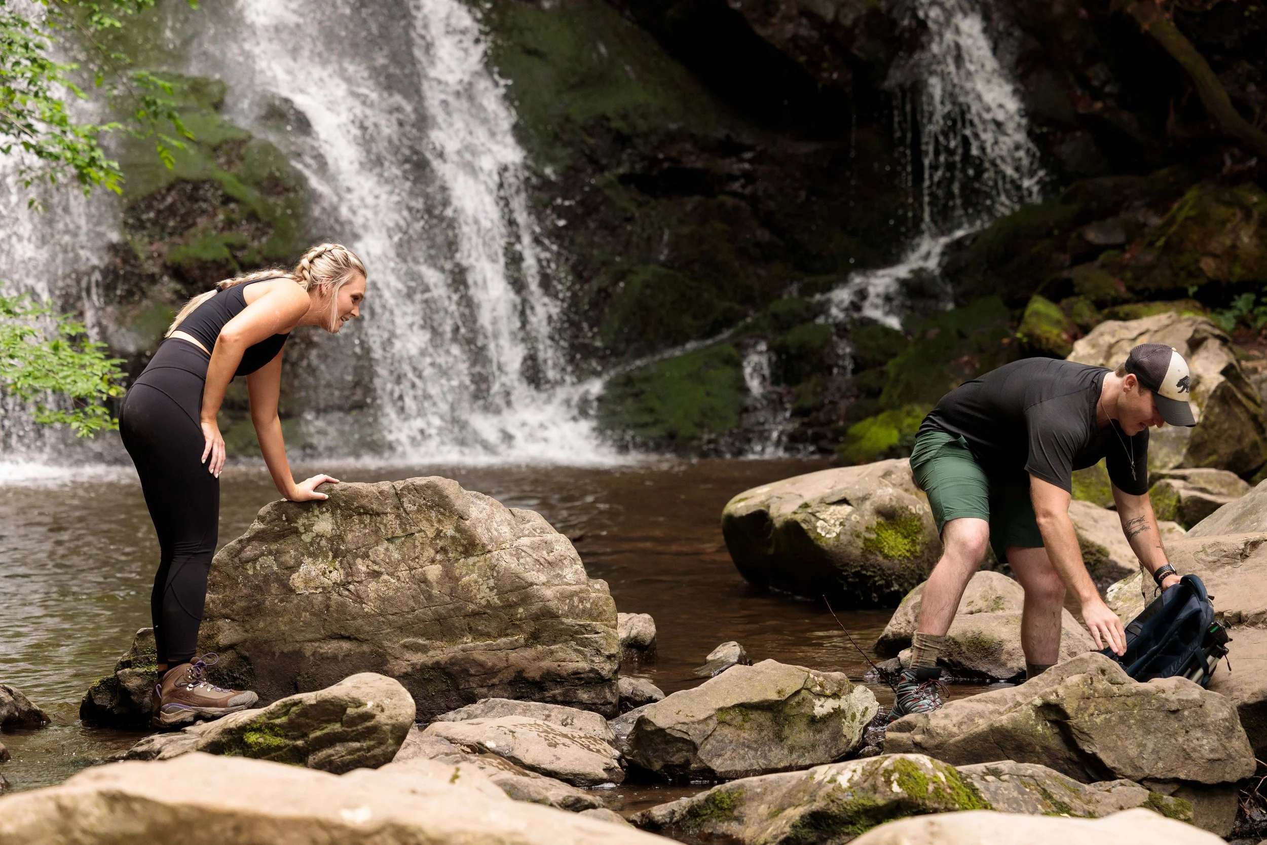 A young athletic couple stes up to take a picture in front of Spruce Flats Falls before a marriage proposal.