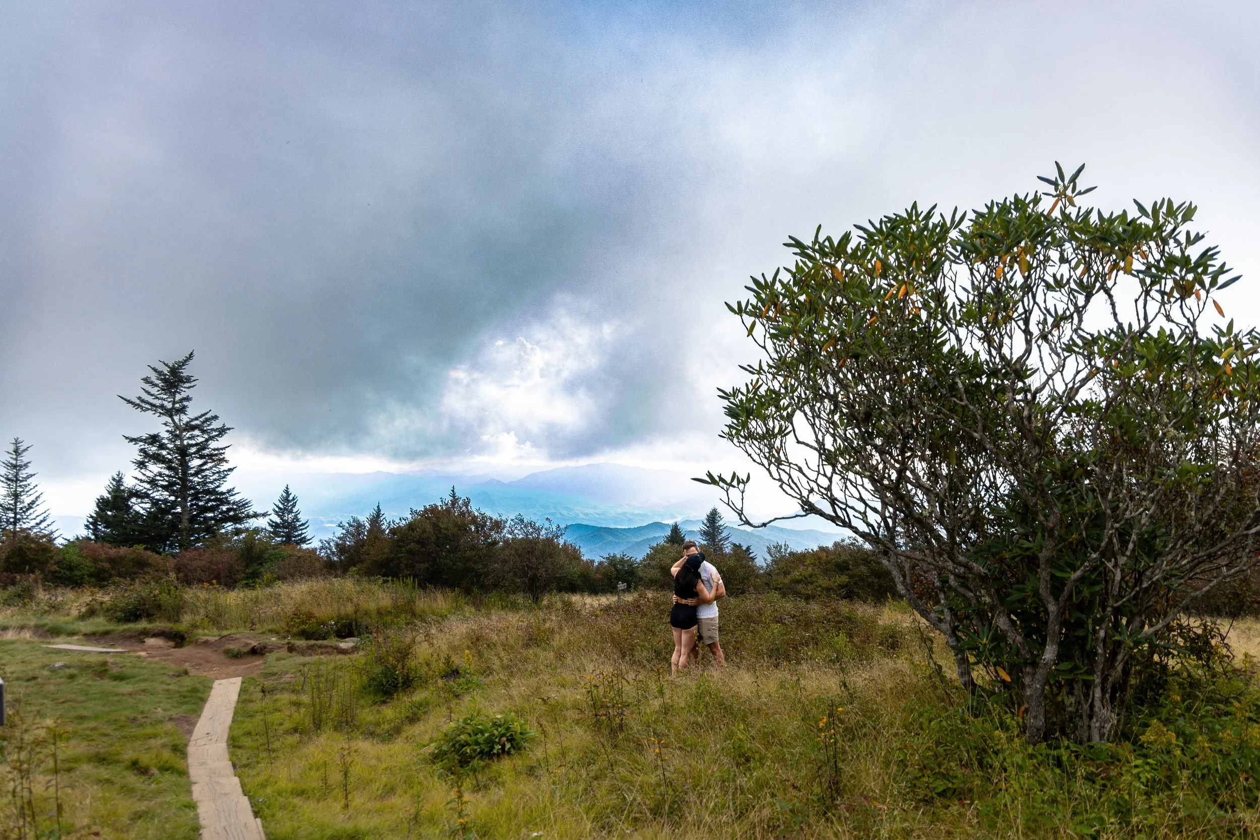 Newly engaged couple embraces beneath dramatic clouds and sweeping mountain views after their Smoky Mountain proposal.