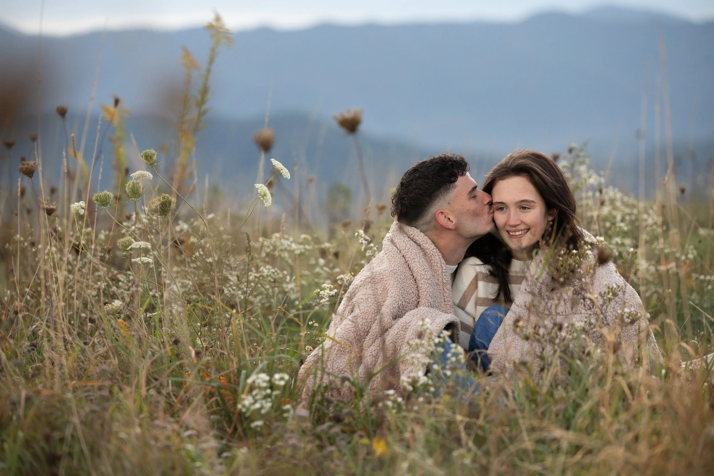 Couple embracing beneath a blanket among golden autumn wildflowers during a Max Patch engagement session.