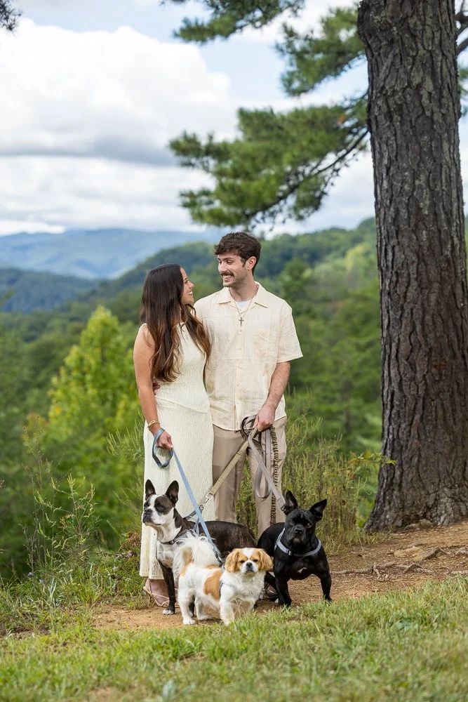 Newly engaged couple standing together with their three dogs at a mountain overlook in the Smokies.