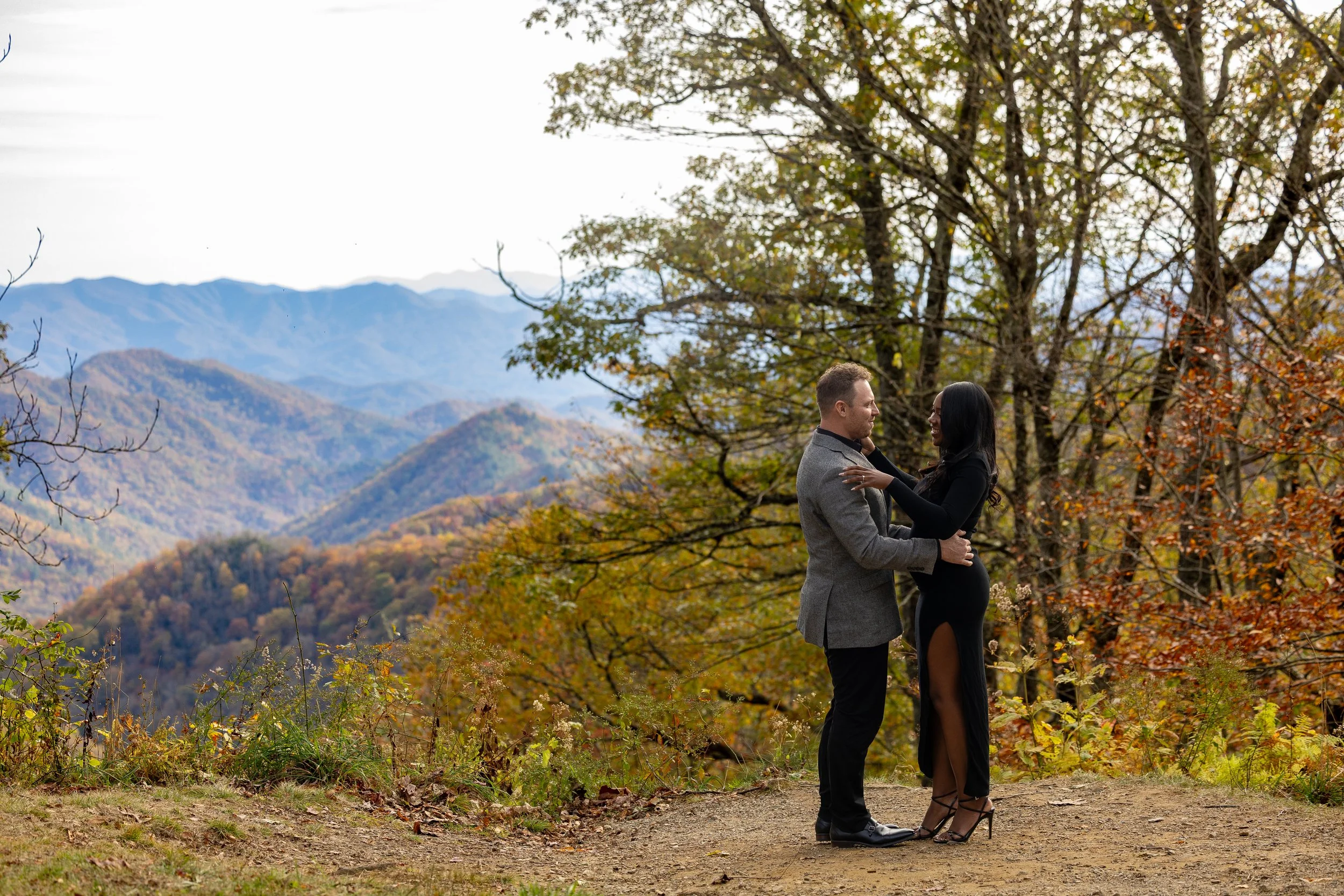 Newly engaged couple embraces at a secluded mountain overlook during peak fall color in the Smokies.
