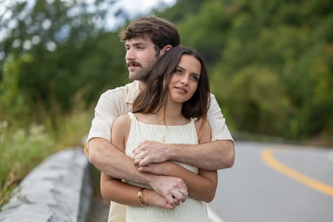 Engaged couple embracing beside a winding mountain road after their Smoky Mountains proposal.