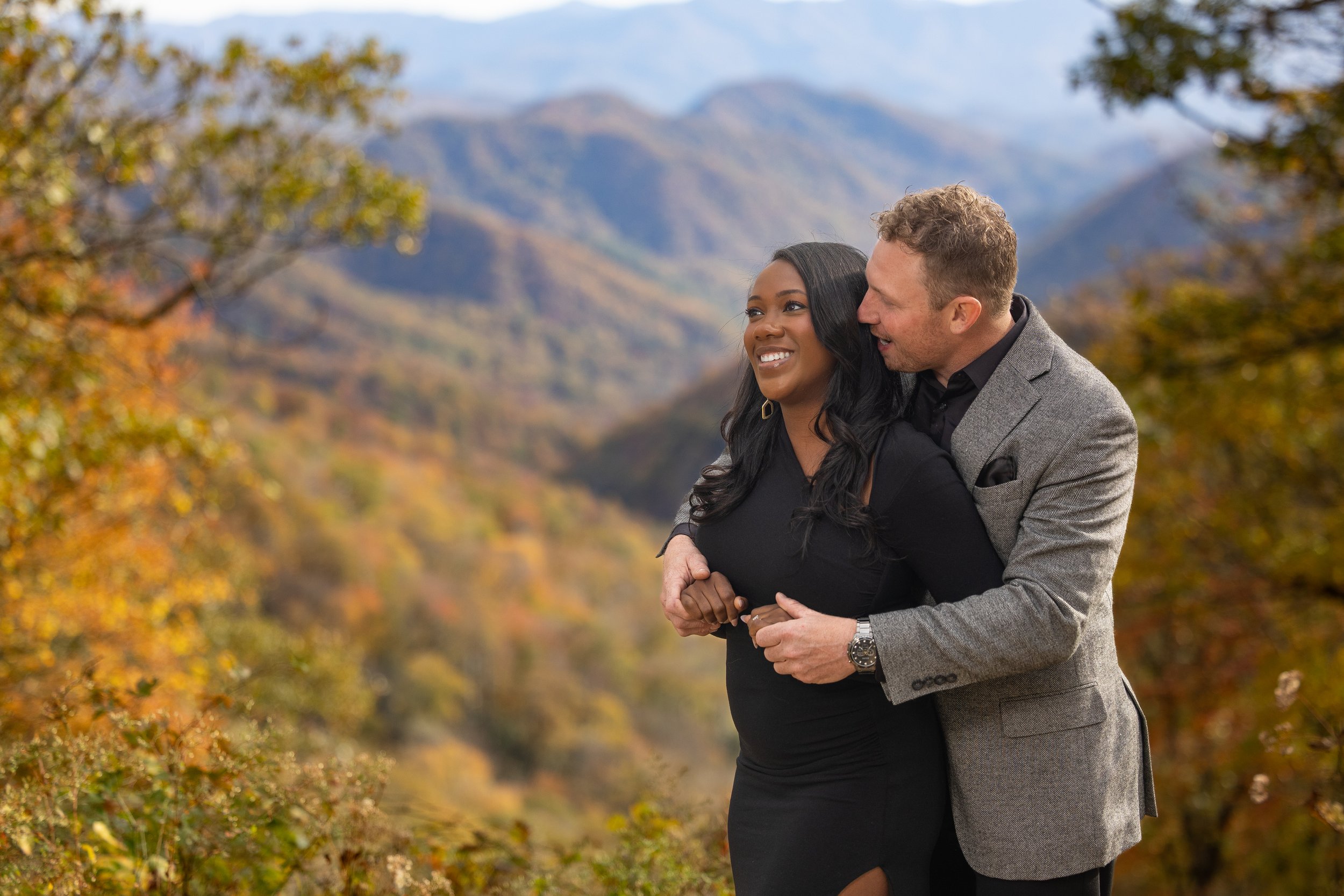 Engaged couple shares a quiet moment against colorful fall mountain scenery in the Smokies.