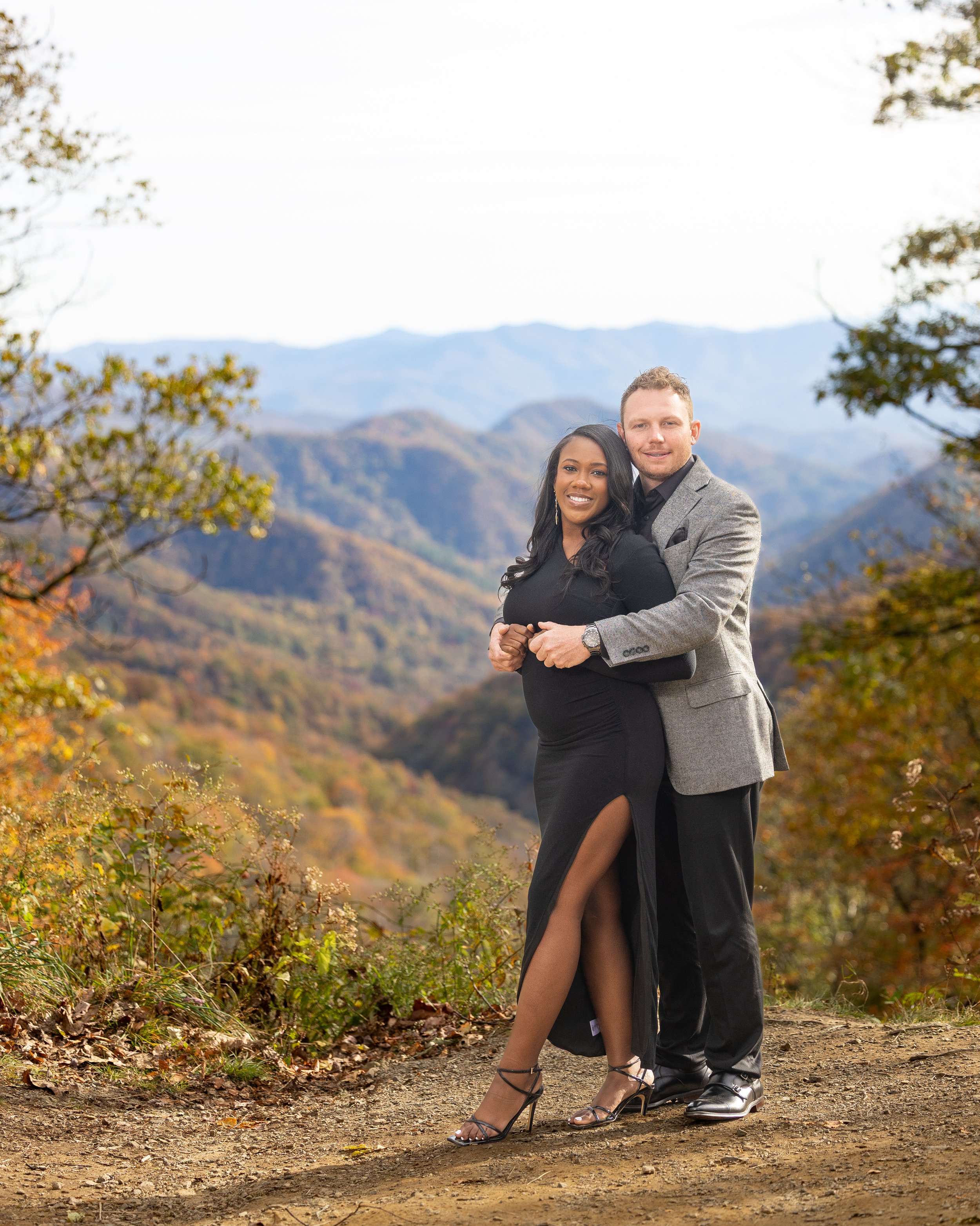 Newly engaged couple poses together with layers of autumn-colored Smoky Mountains in the background.