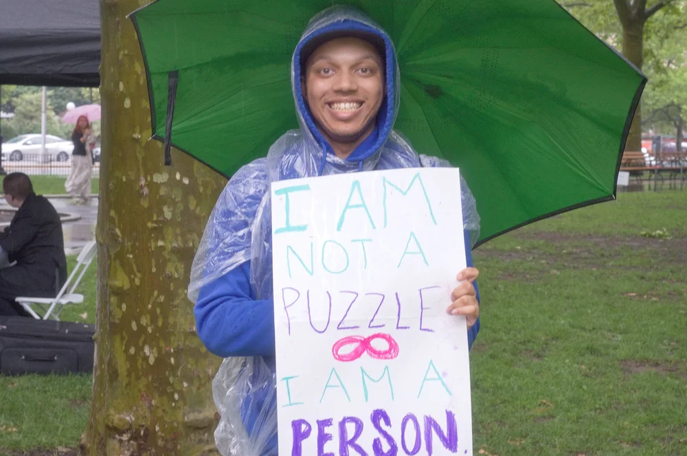  An attendee holds a sign which reads “I am not a puzzle, I am a person” with the infinity symbol for neurodiversity/Autism. 