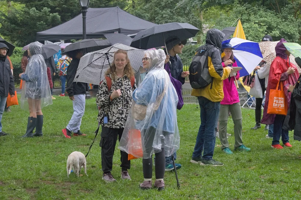  Event attendees gathered and visiting on the grass with umbrellas and rain ponchos. 