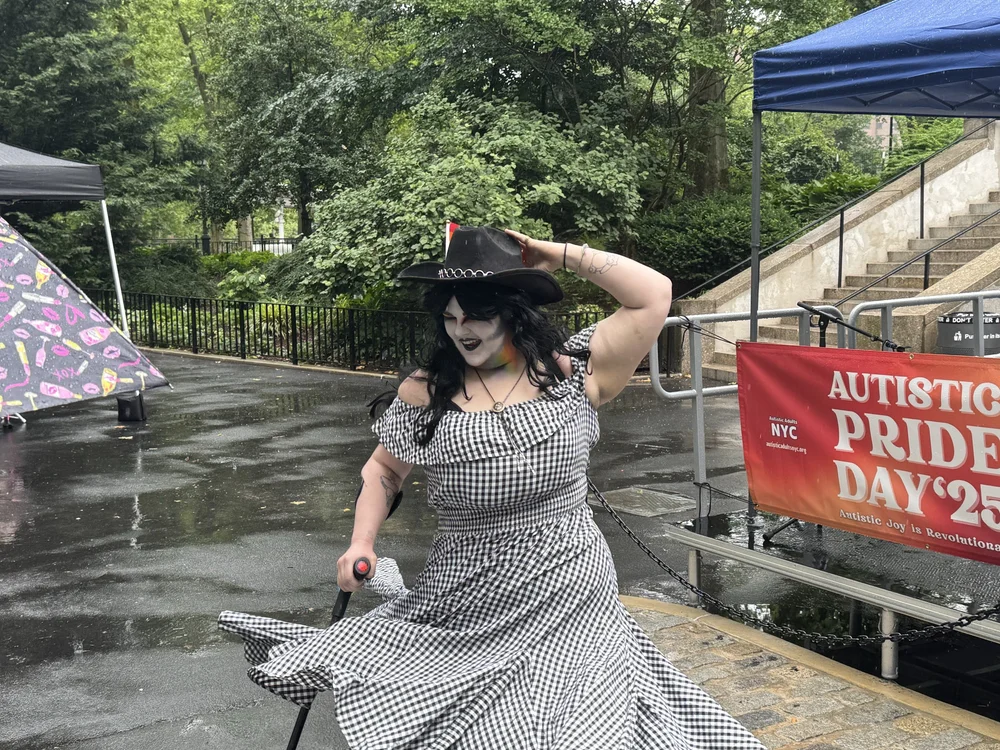  LaHaute Wheels dancing in the rain. They wear a black cowboy hat, dramatic black &amp; white makeup, a matching checkered dress that twirls around them, and a cane. 