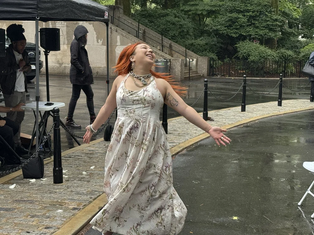  Jennesis Pham twirling in the rain while he looks toward the sky, smiling. 