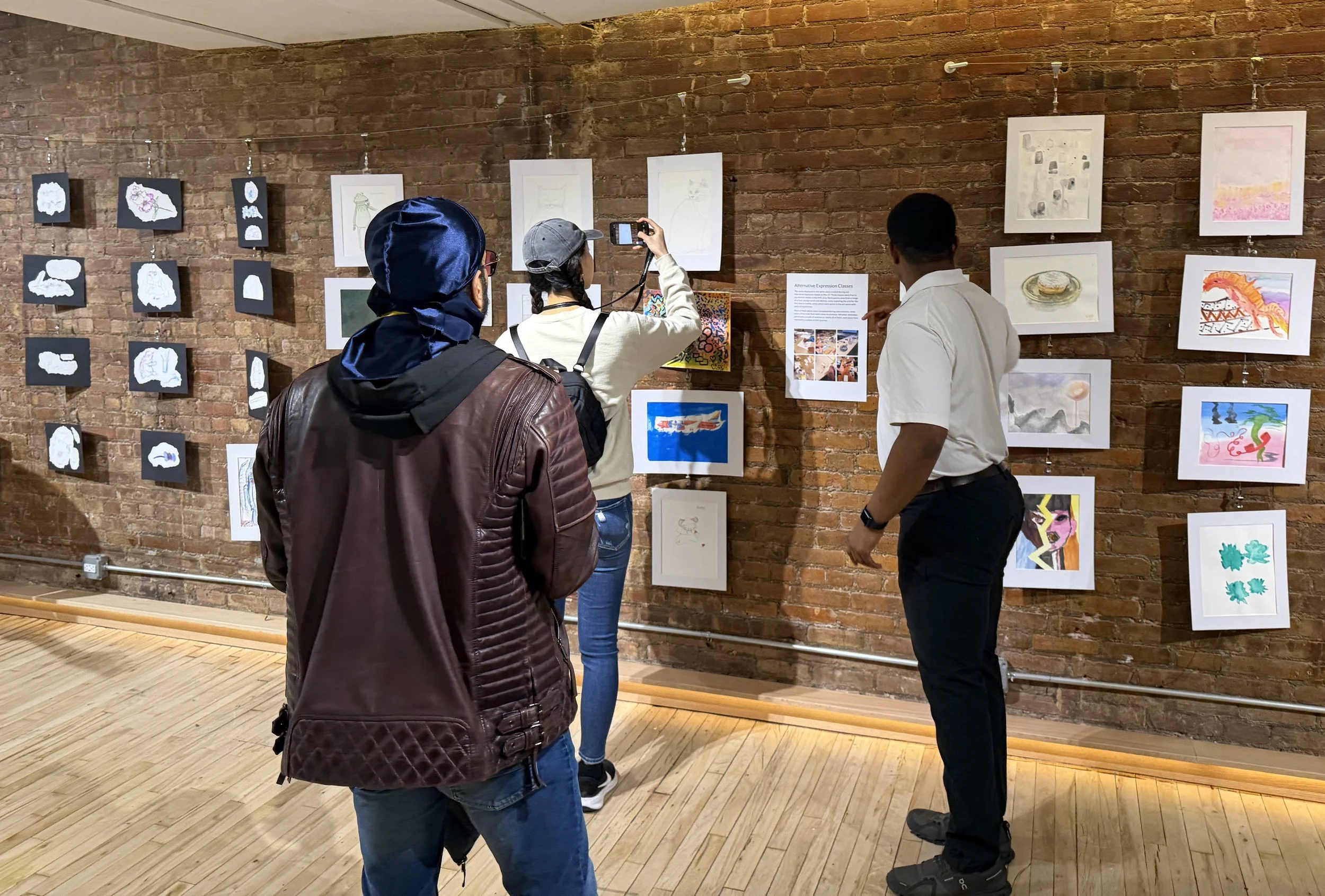  Image of attendees looking at and taking pictures of artworks on wall. 