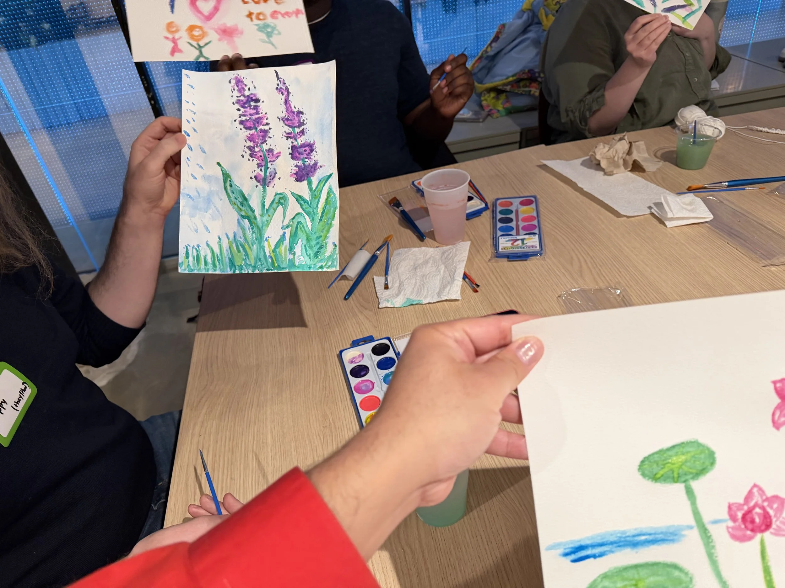  Image of attendees holding up watercolor paintings in progress. 