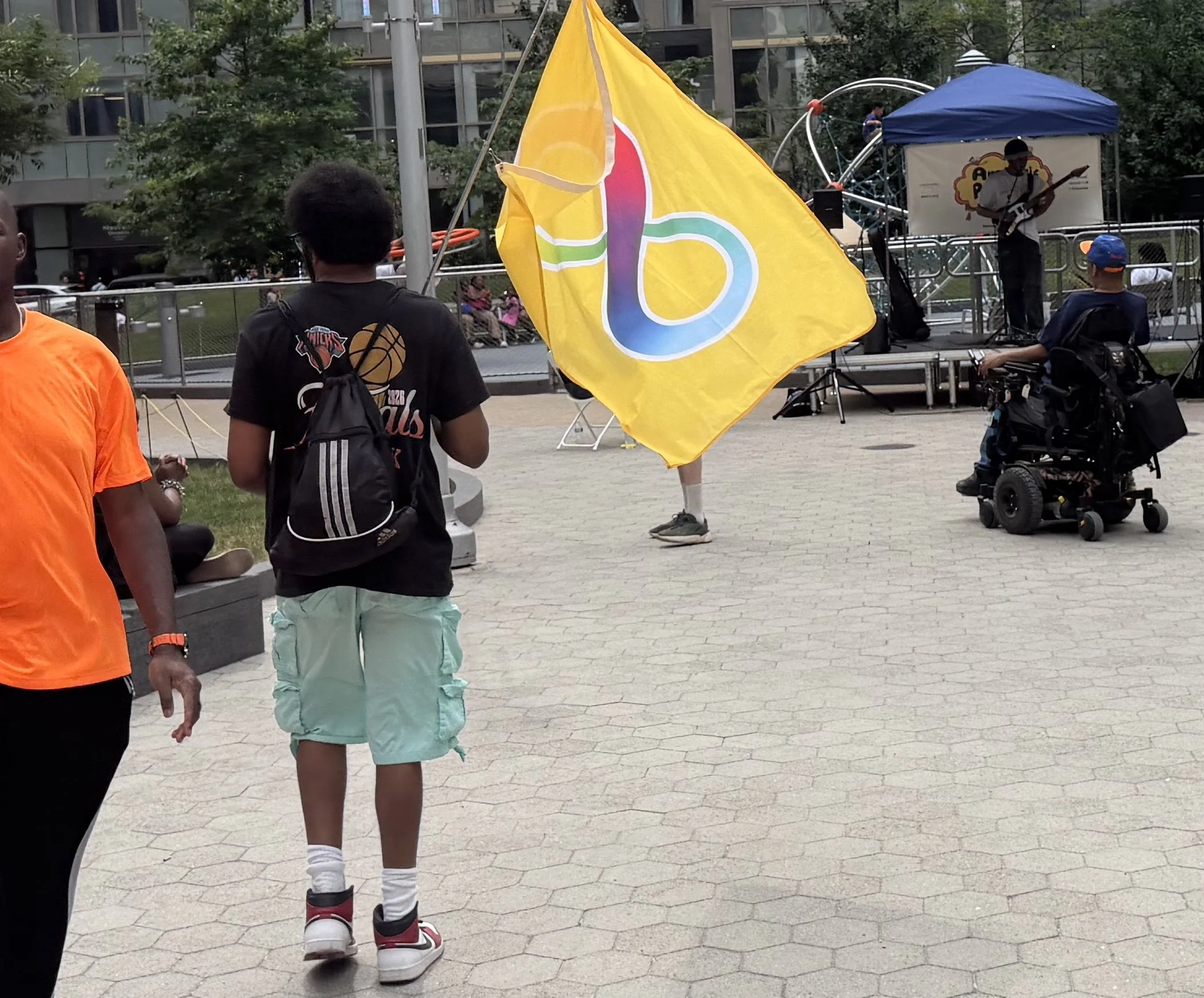  Attendee facing the stage, holding a yellow flag with a rainbow neurodiversity infinity 