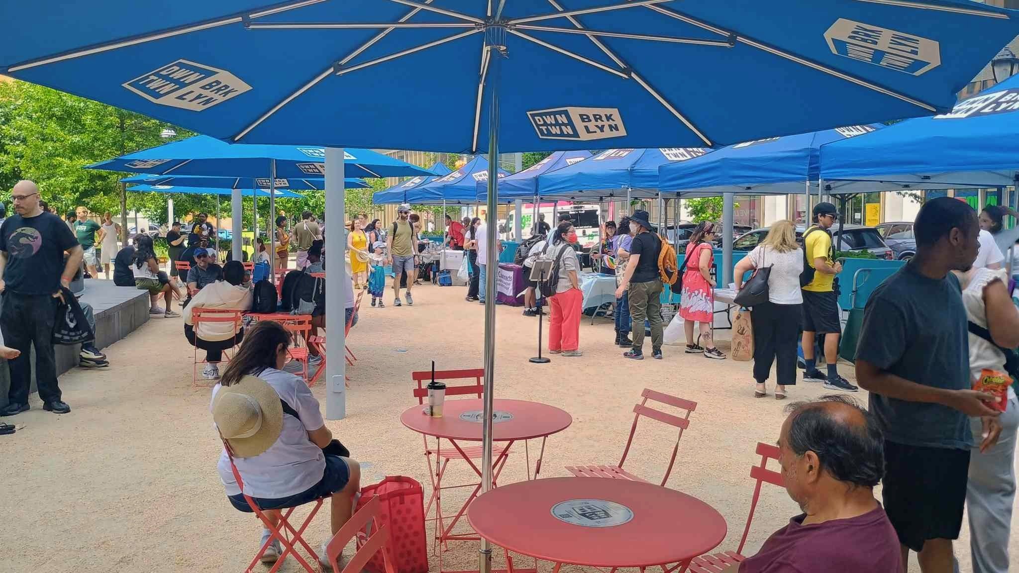  Perspective under a blue umbrella at a red picnic table, facing the crowd 