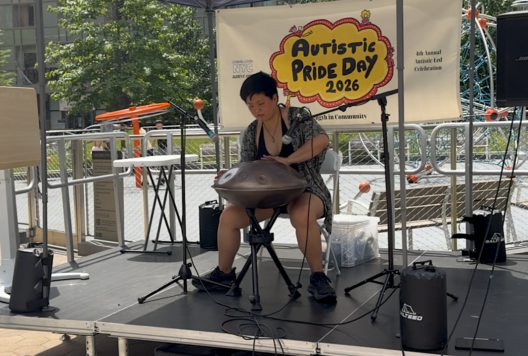  Person seated at the stage with short black hair, playing the handpan instrument 