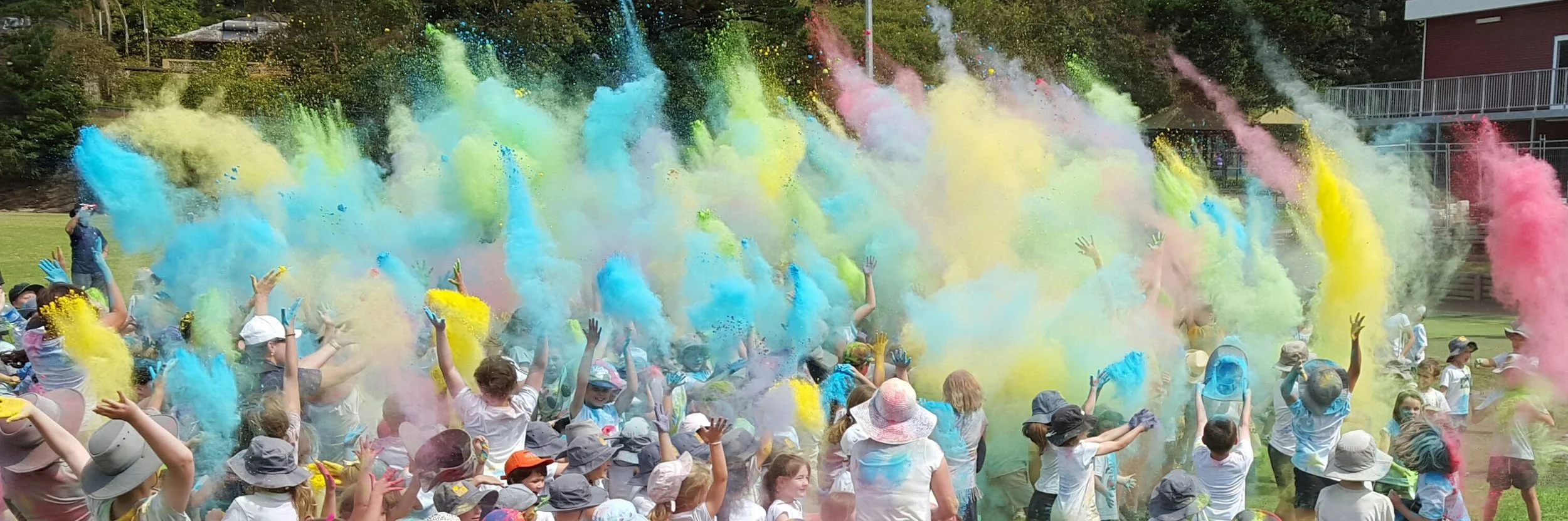 Crowd of children and adults celebrating colorful powder during a Festival of Color event in a park.