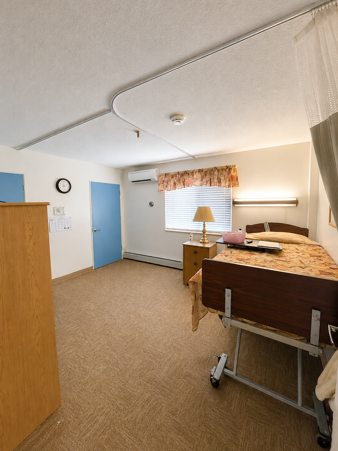 A patient room with a hospital bed, nightstand, lamp, and blue door.