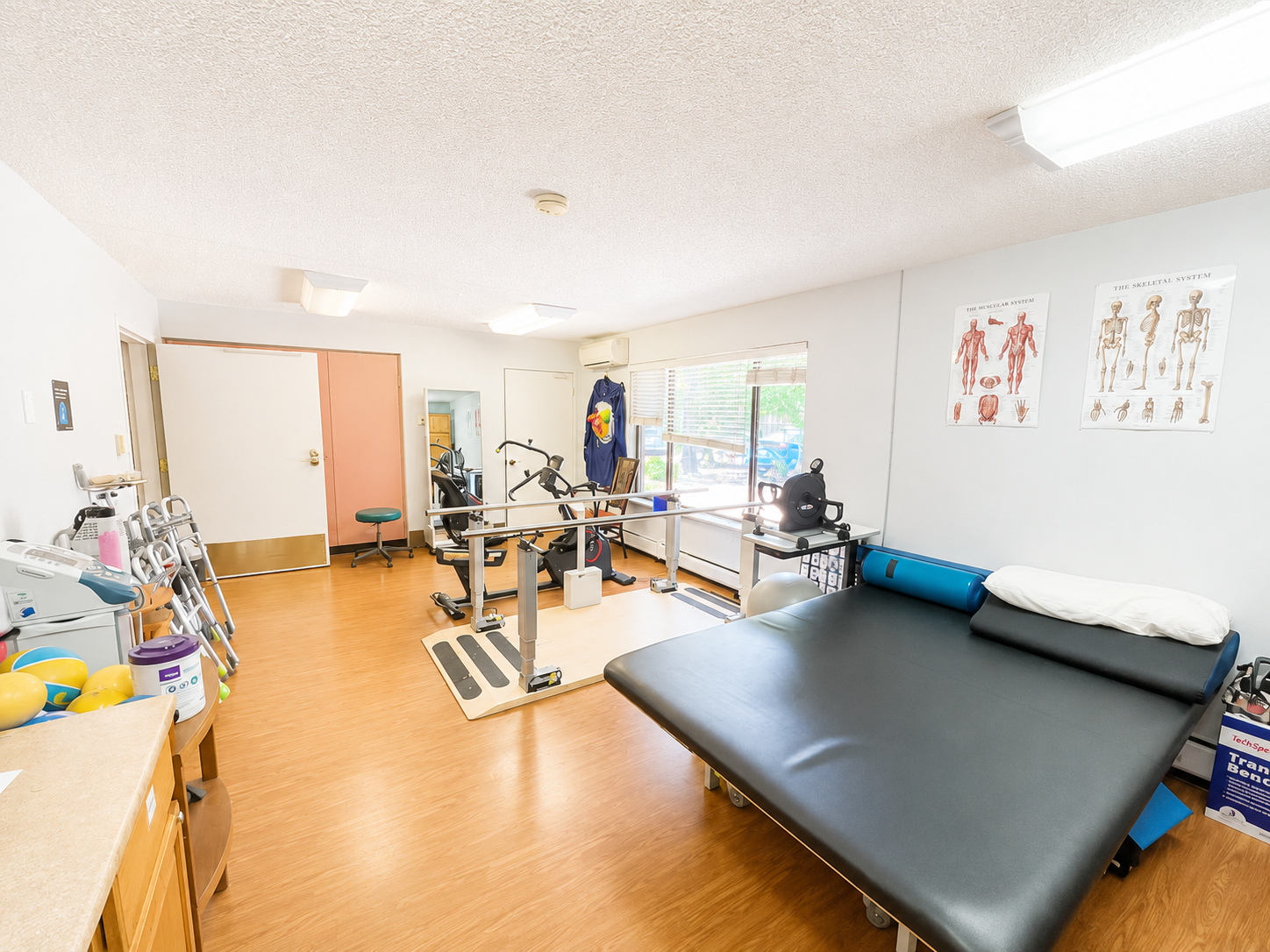 A physical therapy room with parallel bars, exercise equipment, and an treatment table.