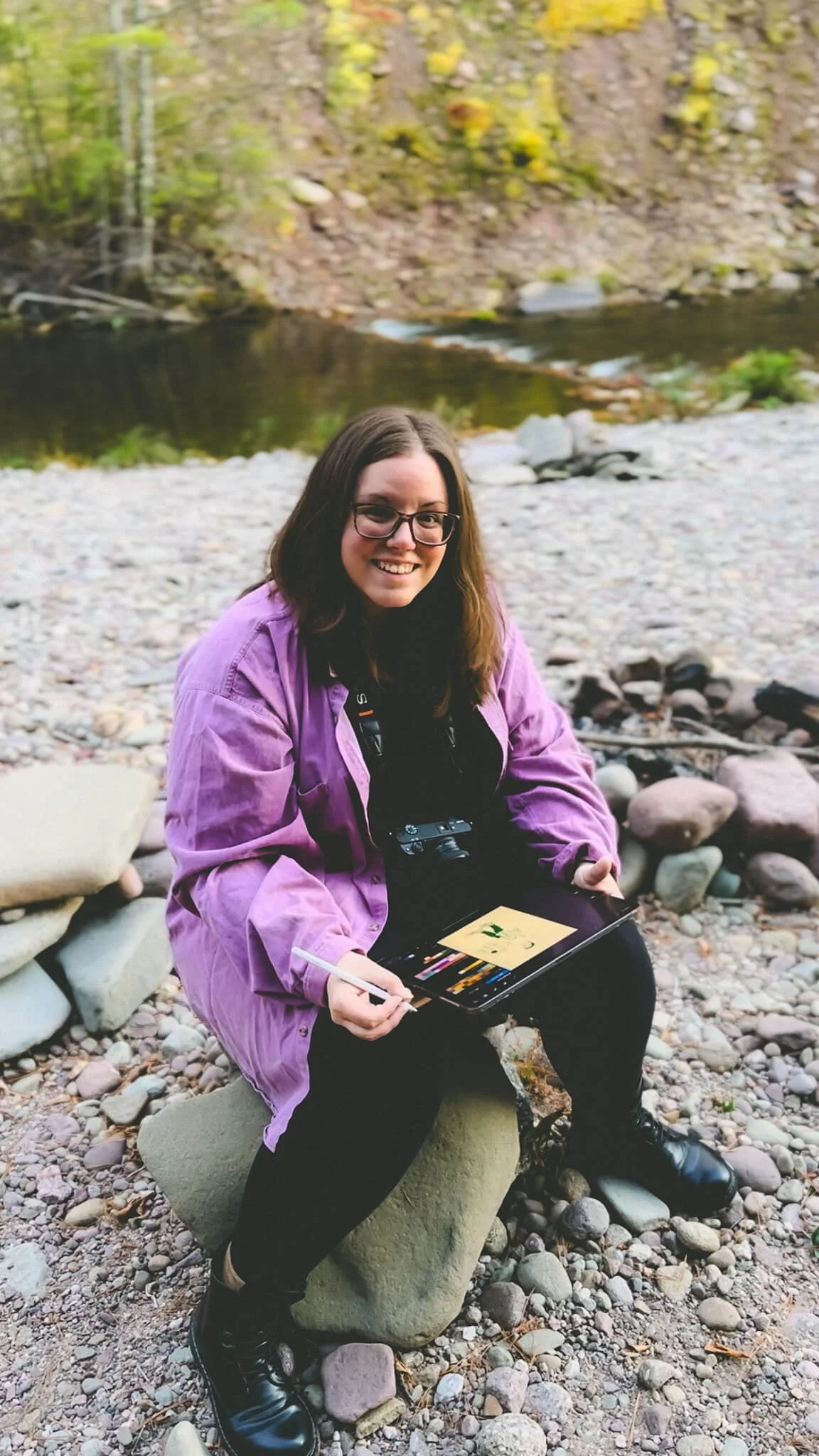 Paxton by a creek drawing on her ipad smiling looking at the camera
