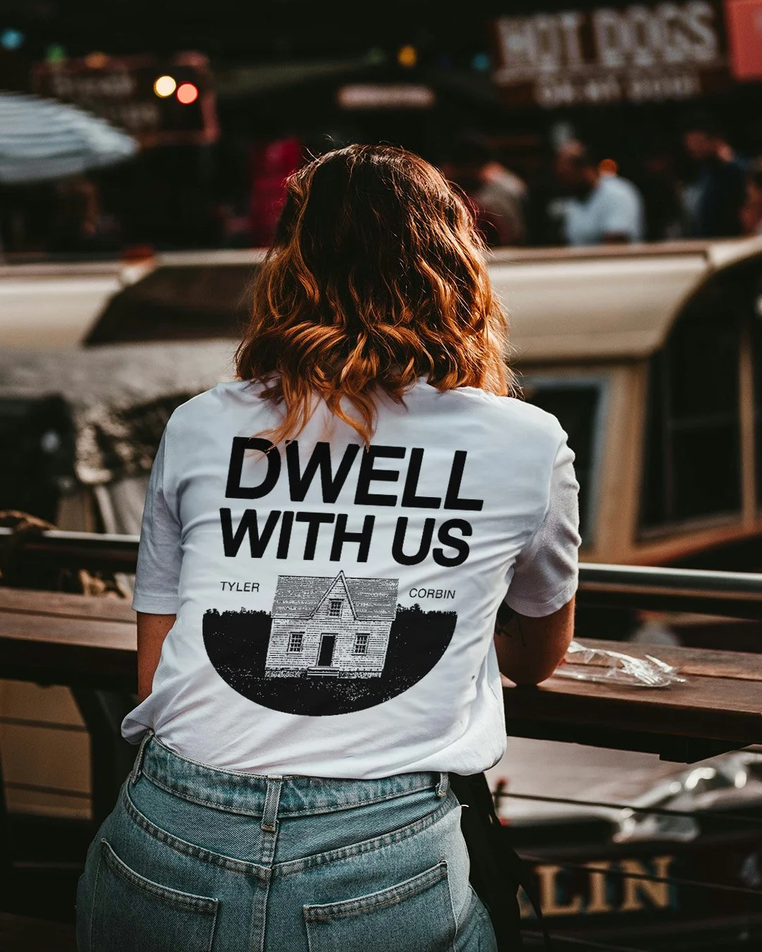 Back of Lady in a white tshirt with the words "Dwell with us" then "Tyler Corbin"