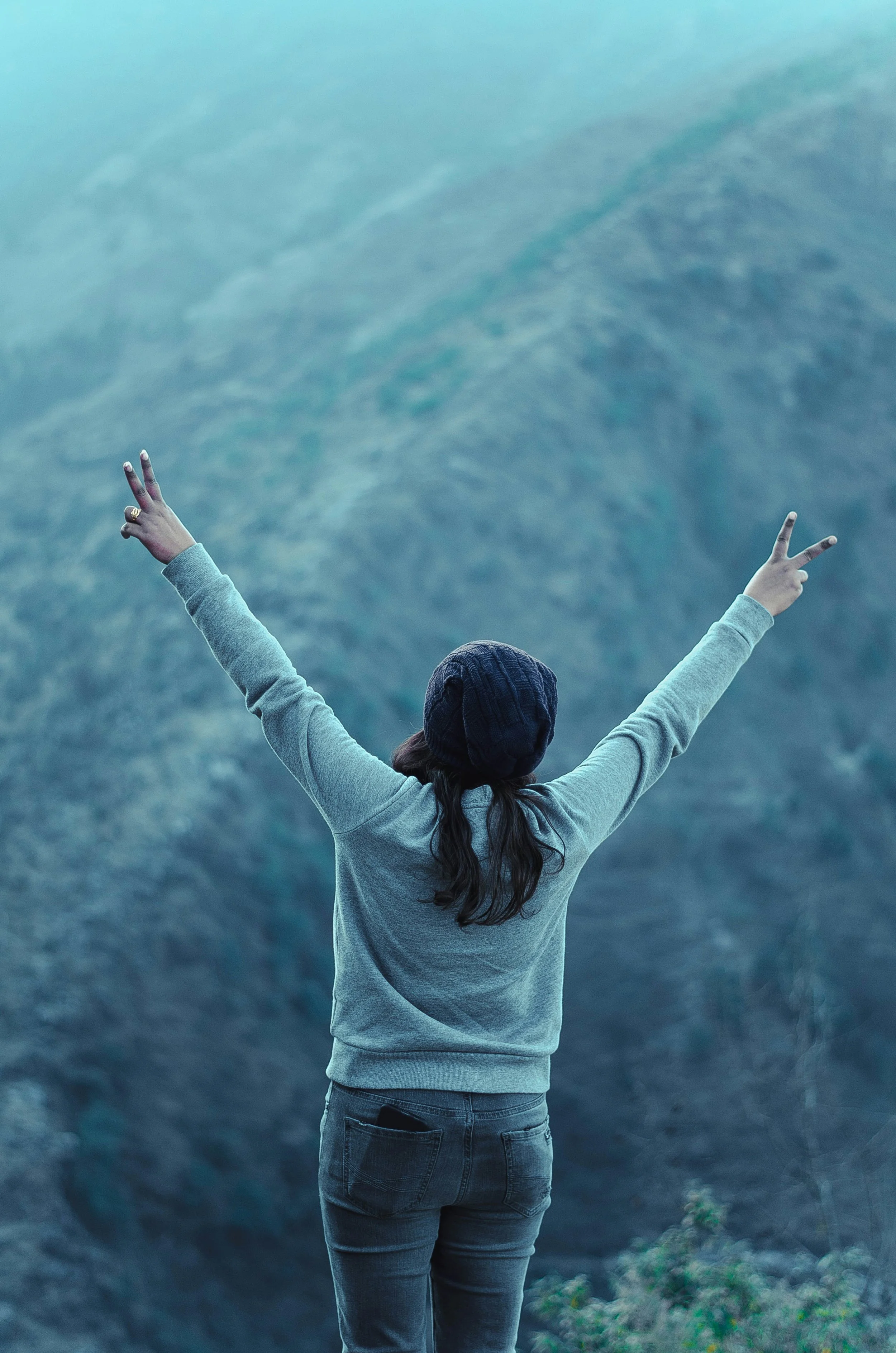 Back view of a person with arms raised in victory sign against a misty mountain backdrop