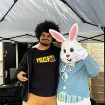 A man standing with the Easter Bunny under a tent.