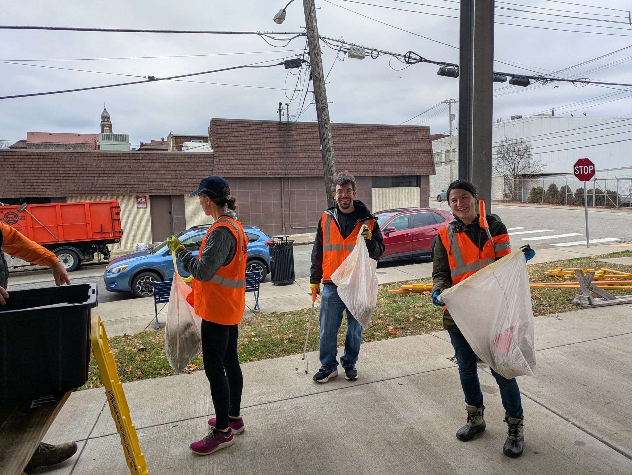 Three volunteers holding trash bags next to a garbage bin for community clean up event.