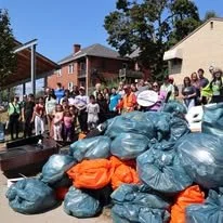 A group of people standing behind a large pile of garbage bags at the City of Pittsburgh's Garbage Olympics. 