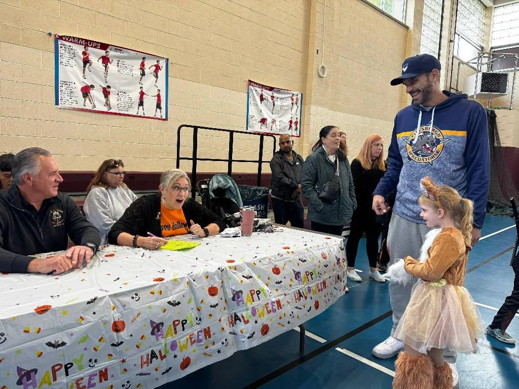 Father and young daughter approaching volunteers at a happy halloween table.