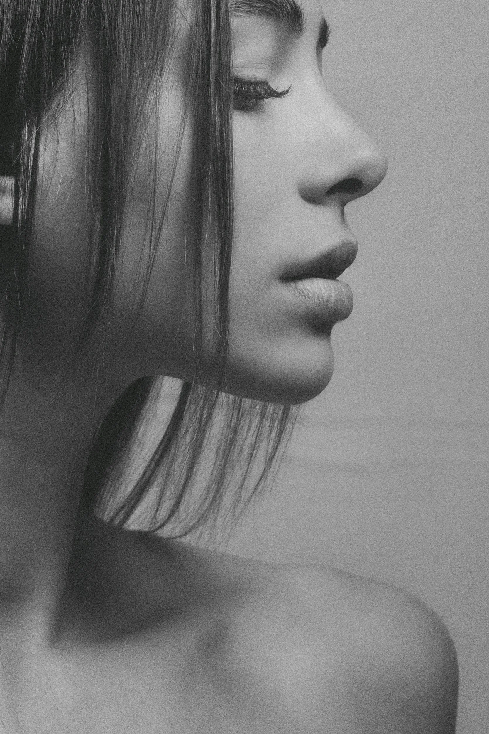 Close-up black and white photo of a woman's face showing her nose, lips, and closed eye, with long hair partially covering her face.