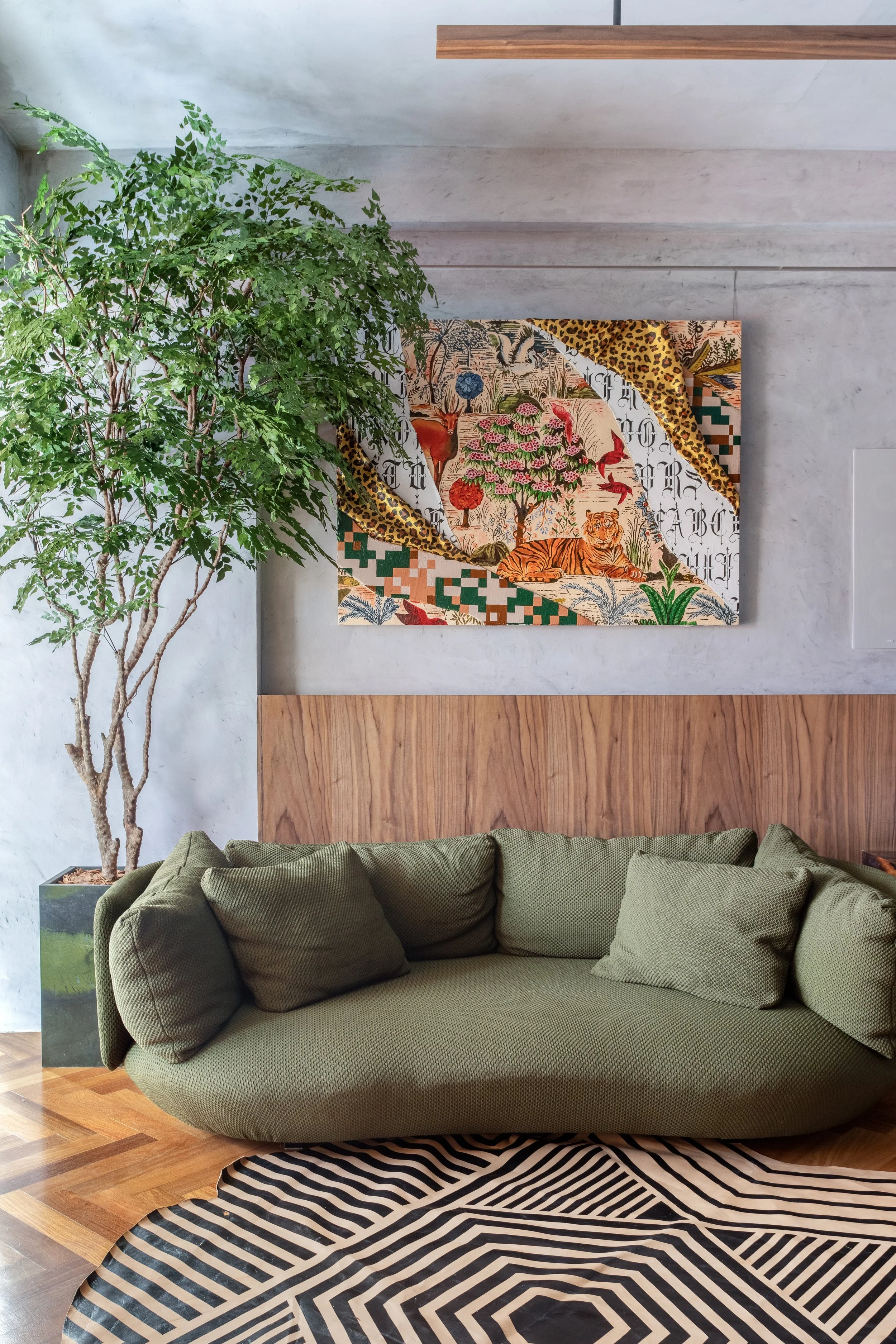 Modern living room with a green sofa, large potted plant, abstract painting, and geometric rug.