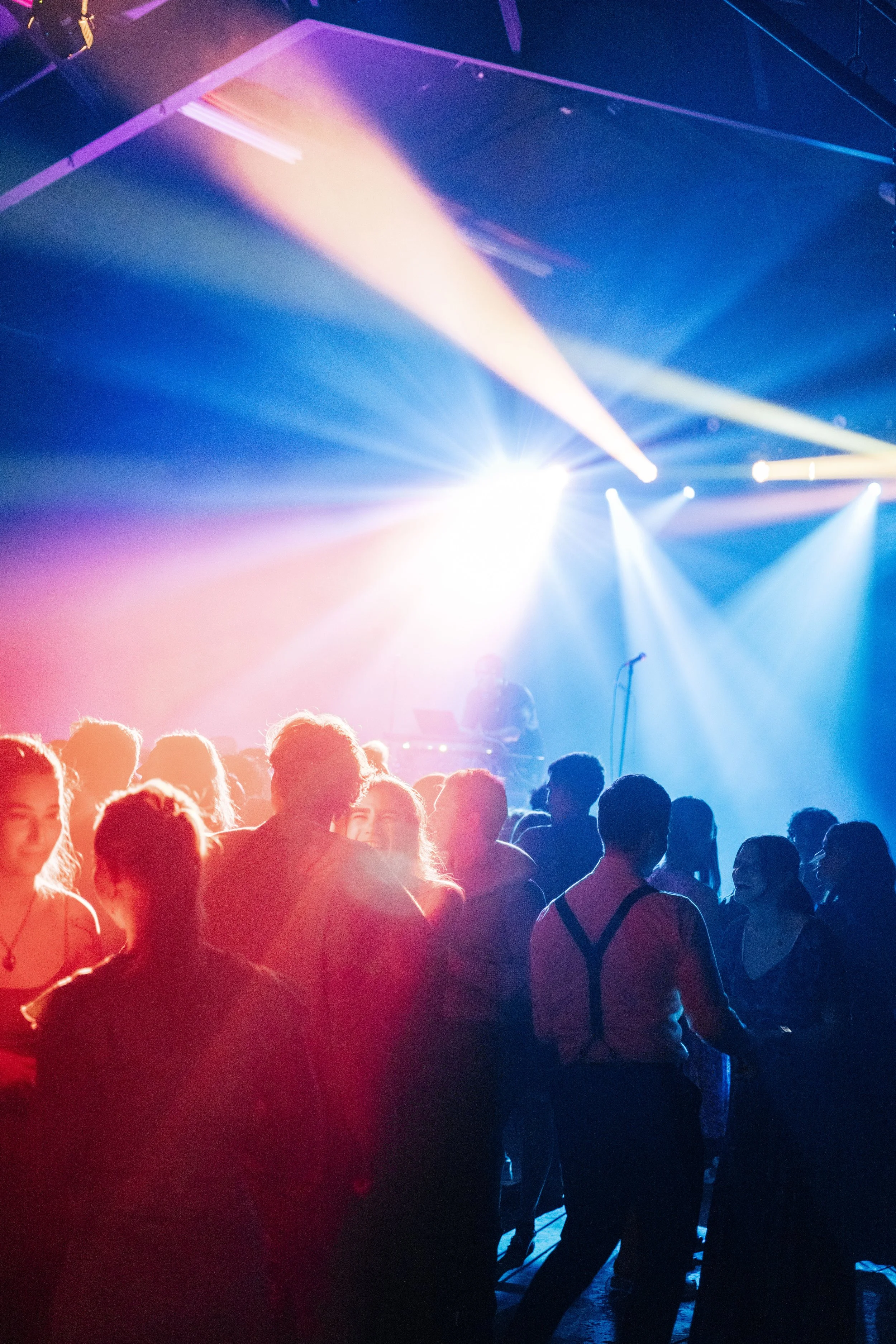 A crowd of people dancing at a nightclub with colorful stage lights and fog creating a lively atmosphere.
