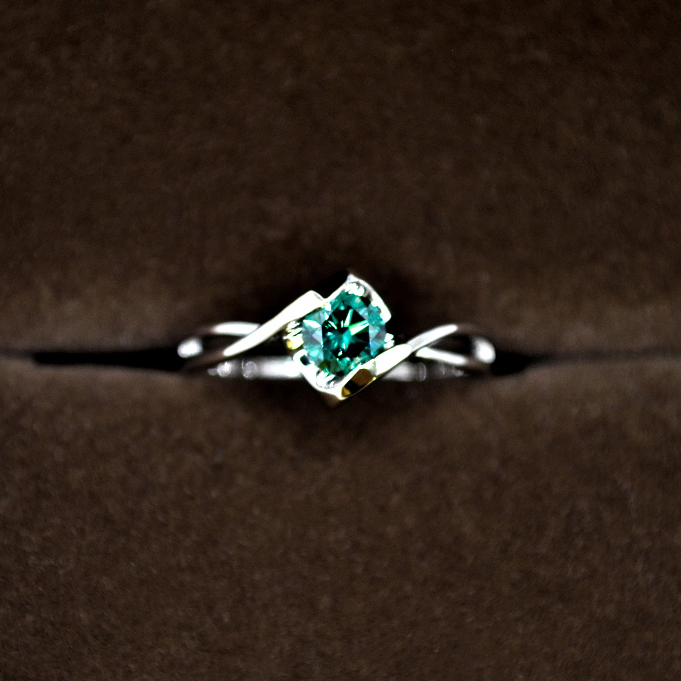 A sleek platinum cremation ring featuring a radiant green diamond, beautifully cradled in an elegant twisted shank design.