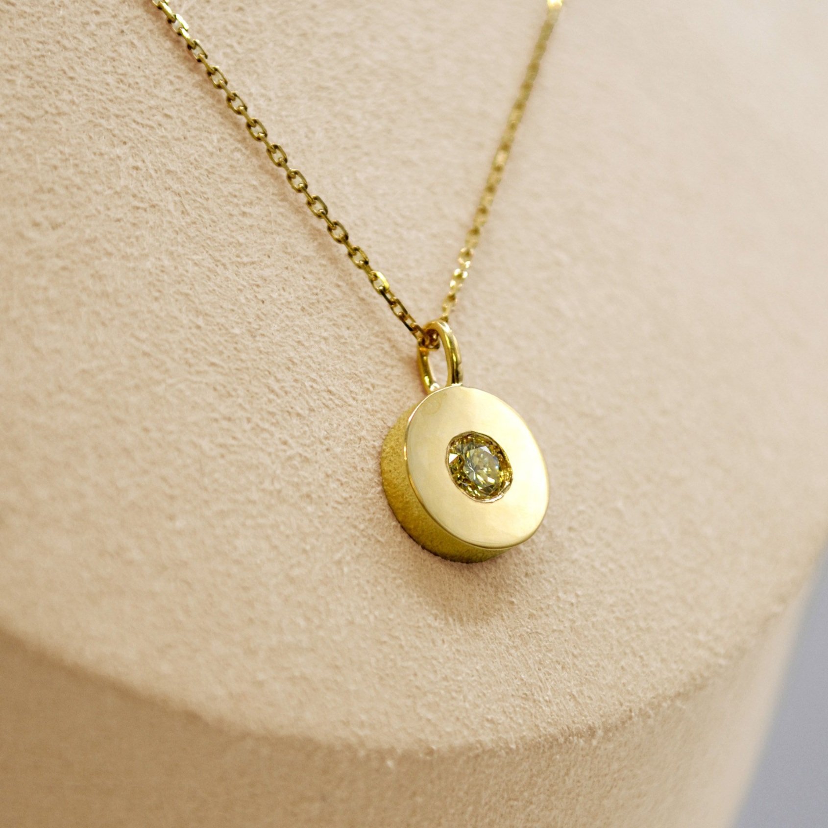 Round, sleek gold pendant with a central diamond, hanging elegantly on a gold chain, for a minimalist and timeless look.