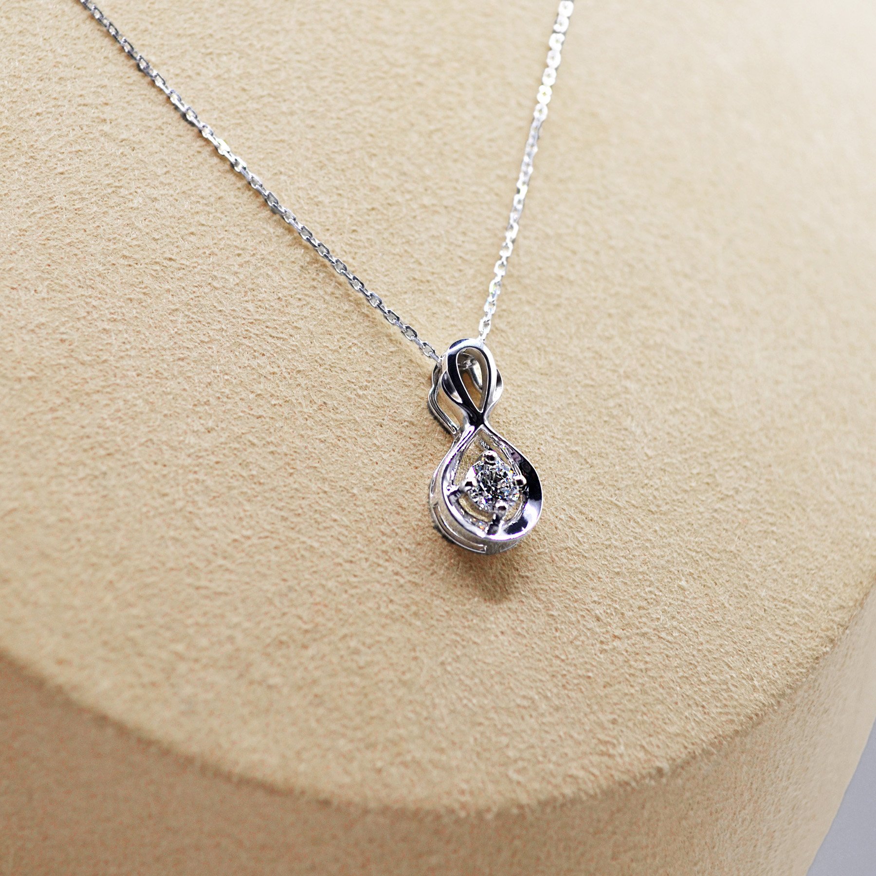 White gold necklace with an infinity drop pendant, featuring a central round diamond, elegantly suspended in a smooth curve.
