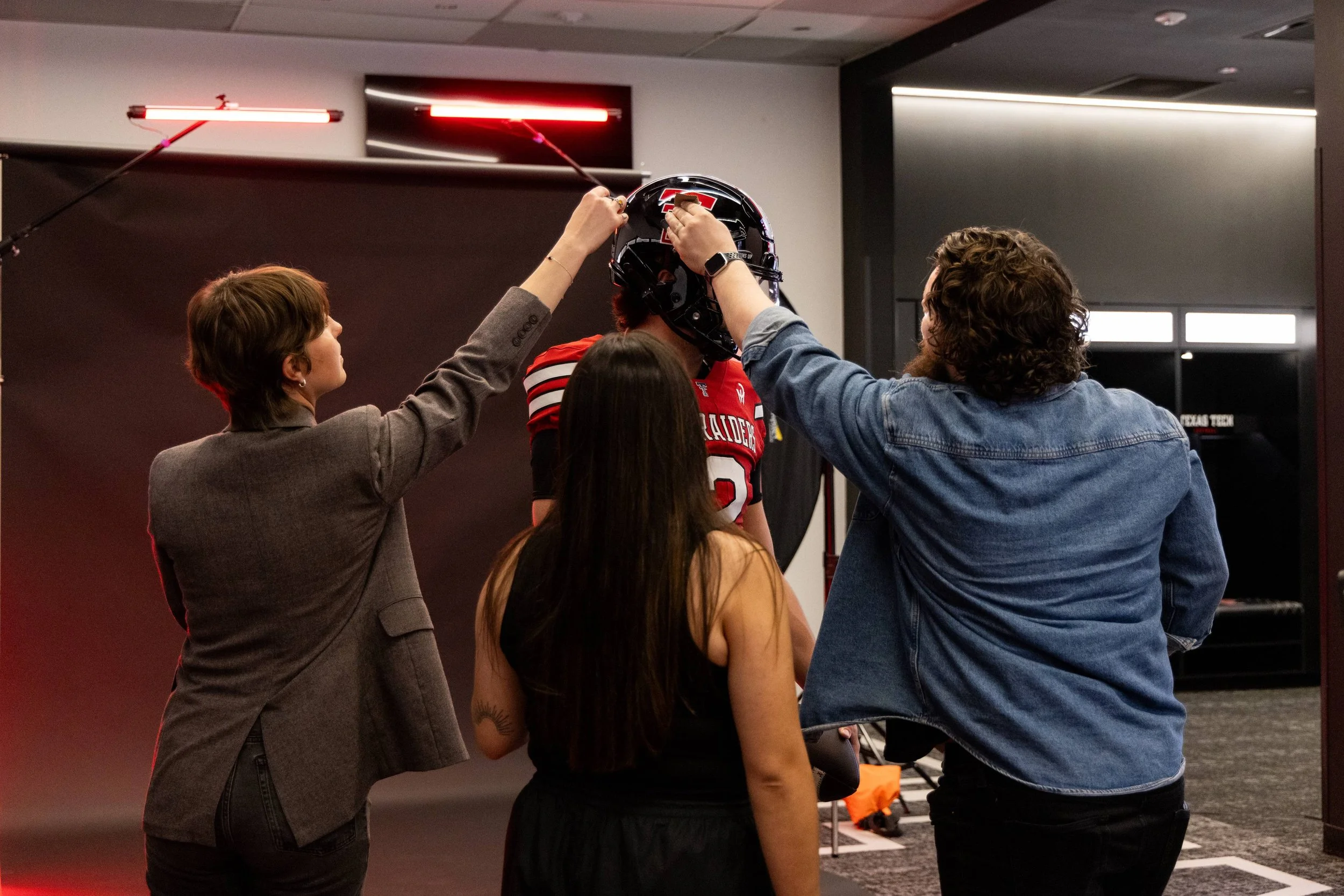 People preparing a football helmet indoors with a Texas Tech logo, under studio lighting.