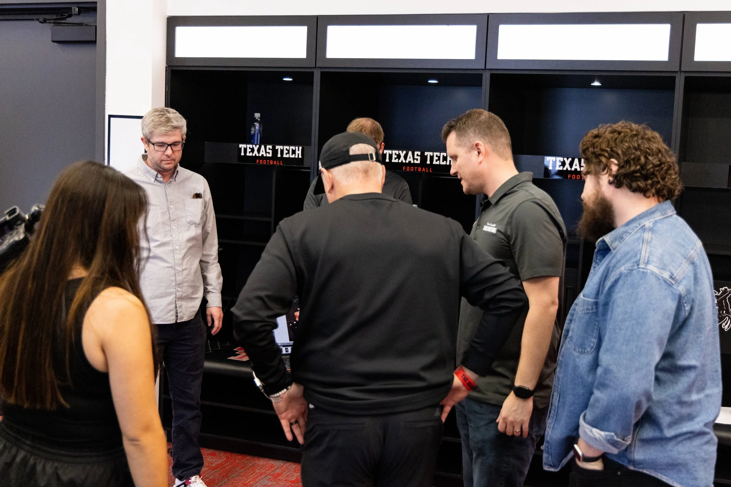 Group of people gathered and talking in a room with Texas Tech Football signs on the background.