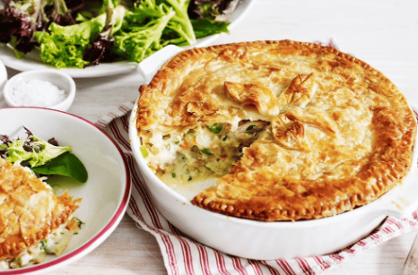 A fish pie with puff pastry top and side salad. Served in a white dish sat on a red and white ticking tablecloth