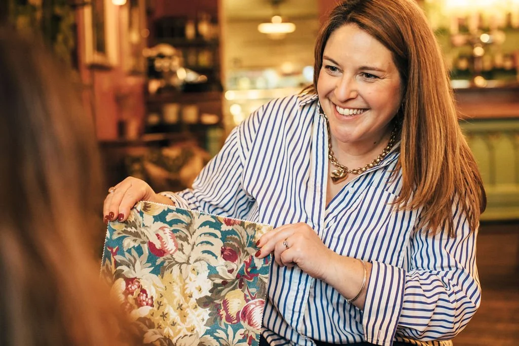 Becky Harrison Interior Designer holding up a velvet fabric sample whilst smiling. She is showing the fabric to another person who is out of shout apart from the side of her head
