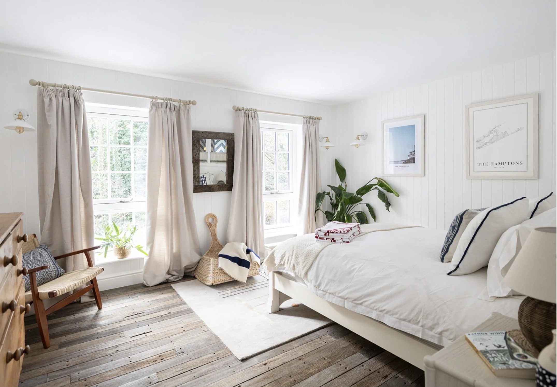 Duel aspect bedroom filled with natural light streaming in through the full height windows. A kingsize bed is pushed against the wall. All walls are panelled and painted white with a wooden floor