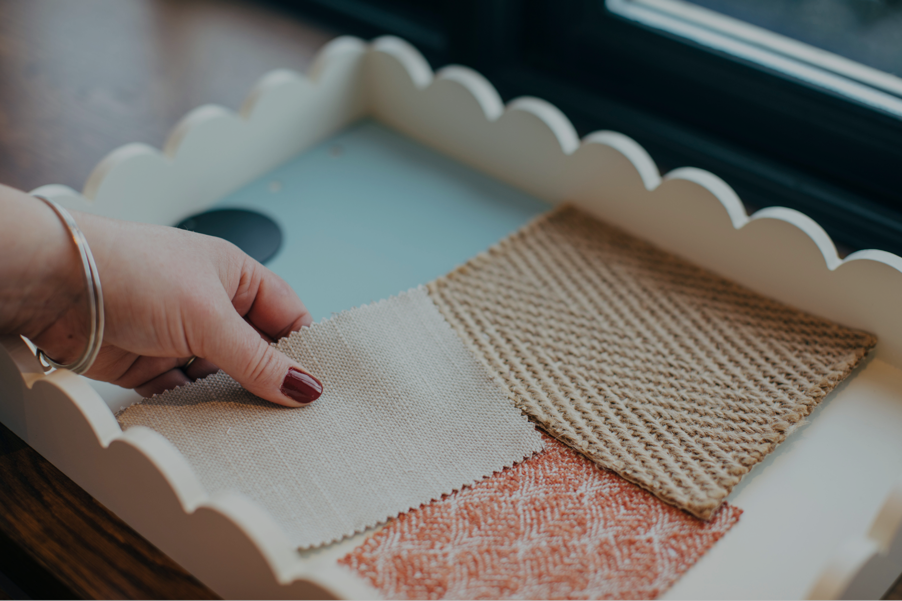 A woman hand over a white tray with interior design samples; fabric, flooring & paint