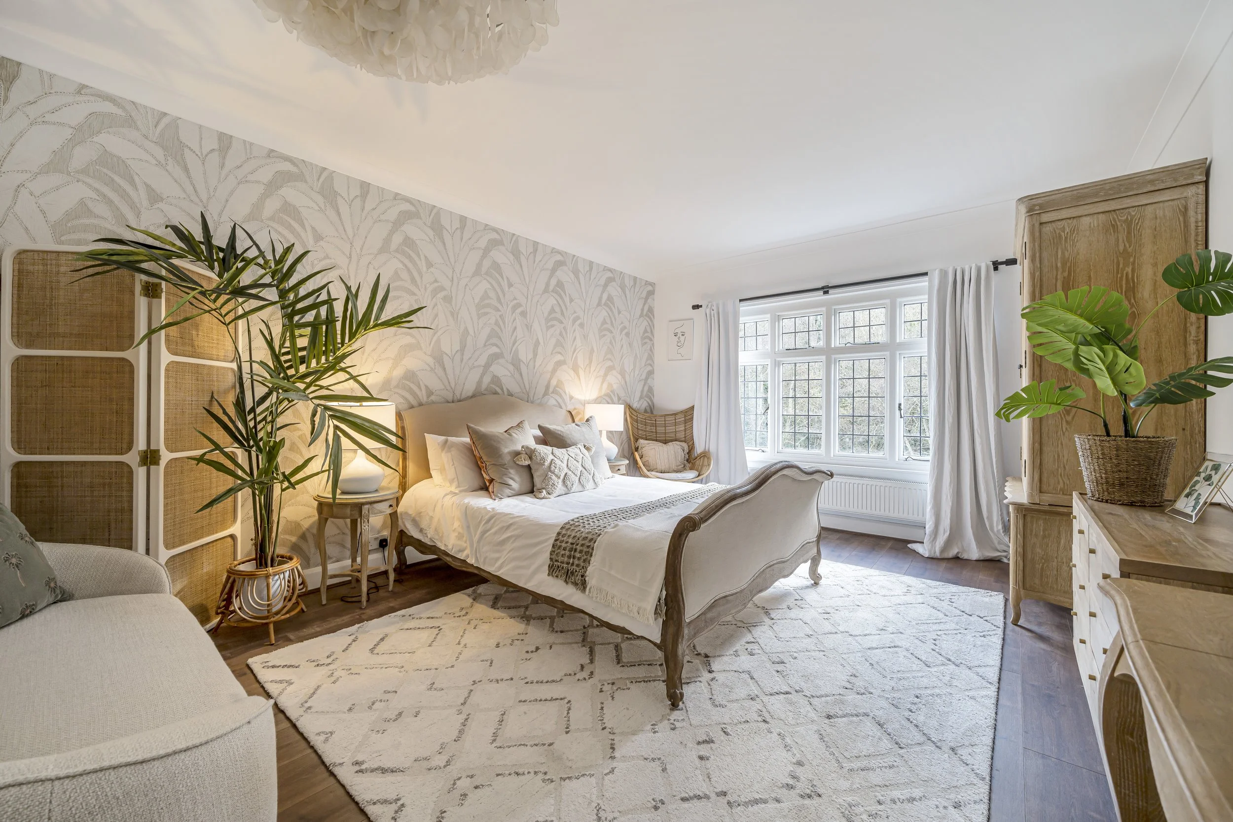 A cosy looking nesutral bedroom with a wallpaperd feature wall behind the bed. It is decorated in a netrual tones with lots of dark wood and plants