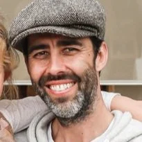 A smiling man with a beard wearing a gray cap.