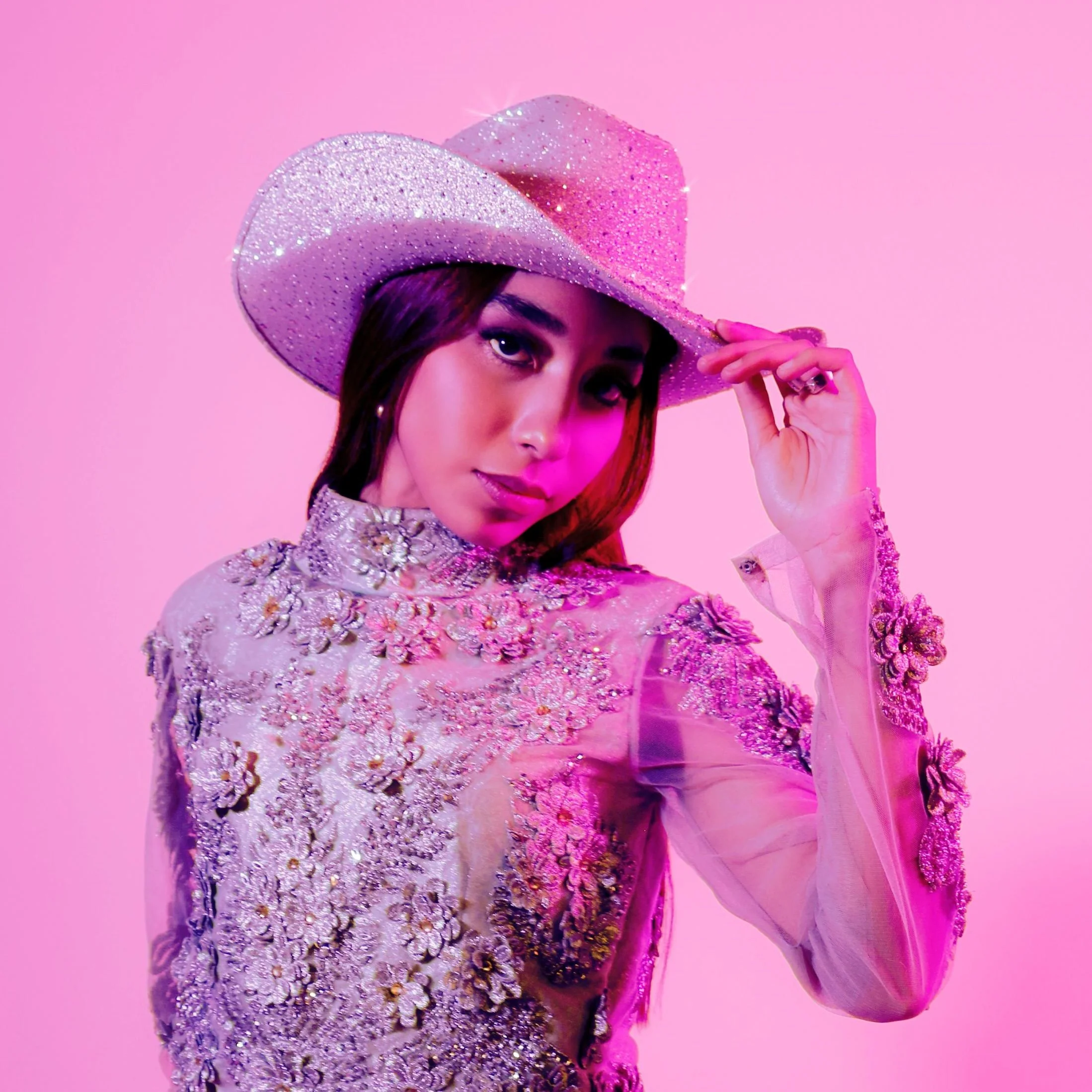 Mujer con sombrero de информация y vestido brillante sobre fondo rosa.